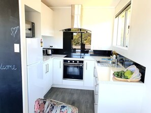 Een moderne keuken met witte kastjes, een zwarte kookplaat en een raam met uitzicht op bomen.