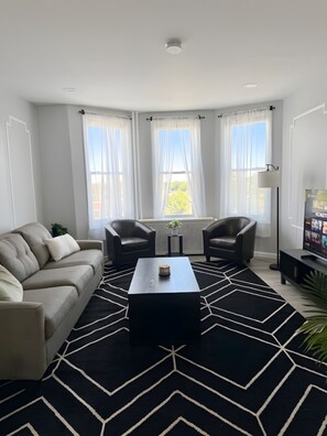 Ein modernes Wohnzimmer mit einer Couch, zwei Sesseln, einem Couchtisch und einem Fernseher.