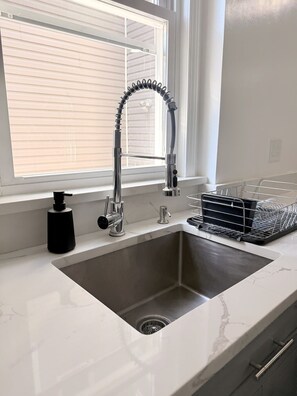 Eine Spüle mit einem modernen Wasserhahn, einer Seifenspender und einem Geschirrgestell.