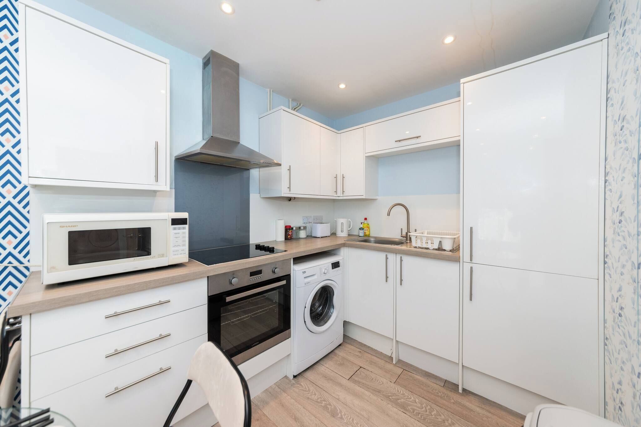A compact kitchen with white cabinets, a microwave, a stove, and a washing machine.