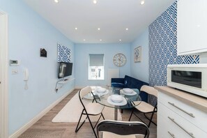 A modern kitchen with a microwave, a dining table with chairs, a blue sofa, and a clock on the wall. - Free Parking Central Reading Flat Fully Equipped (Berkshire)