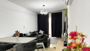 Uma sala de estar moderna com um conjunto de sofá, uma mesa de jantar com cadeiras, um candelabro e um aparador com uma planta.
