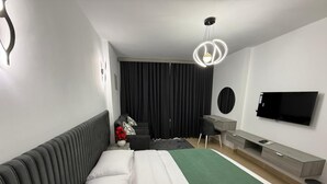 Quarto de hotel moderno com uma cama, escrivaninha, cadeira, televisão e uma janela grande com cortinas.