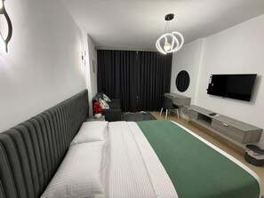 Ein modernes Hotelzimmer mit einem Bett, einem Schreibtisch, einem Sessel, einem Fernseher und einem großen Fenster mit Vorhängen.