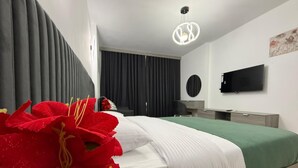 Quarto moderno com cama, televisão de tela plana, escrivaninha e uma janela grande com cortinas.
