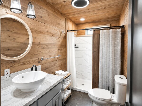 Une salle de bain moderne avec un intérieur en bois, un miroir rond, un lavabo blanc, une douche avec une porte en verre et des toilettes.