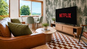 A living room with a leather sofa, a coffee table, a TV displaying 'NETFLIX,' and a patterned wallpaper. - NEW Cabin Olympus: Starlink, Firepit, BBQ (Beaver)