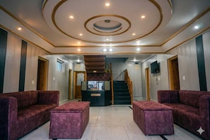 A lobby with a reception desk, two sofas, a staircase, and a clock on the wall. - Classic Pine Hills (Srinagar)