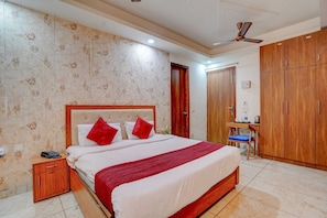 A hotel room with a large bed, a desk, a wardrobe, and a ceiling fan. - Classic Pine Hills (Srinagar)
