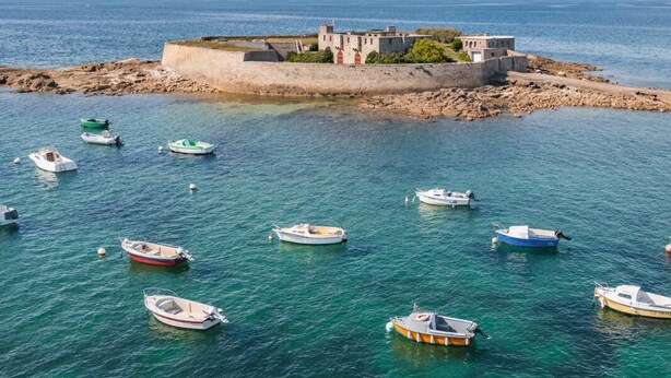 Un paysage côtier avec des bateaux ancrés près d’une structure fortifiée.