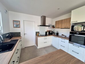 A modern kitchen with white cabinets, a black stove, and a wooden countertop. - Family home in the village (Guidel)