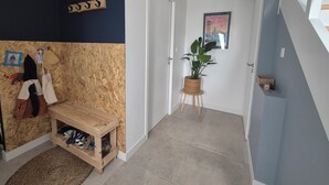 Un couloir avec un banc en bois, une plante en pot, un porte-manteau et un tableau encadré accroché au mur.