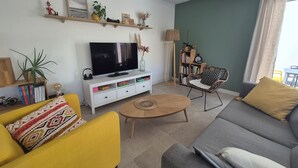 Un salon comprenant un téléviseur, un canapé, un fauteuil, une bibliothèque et une petite table.