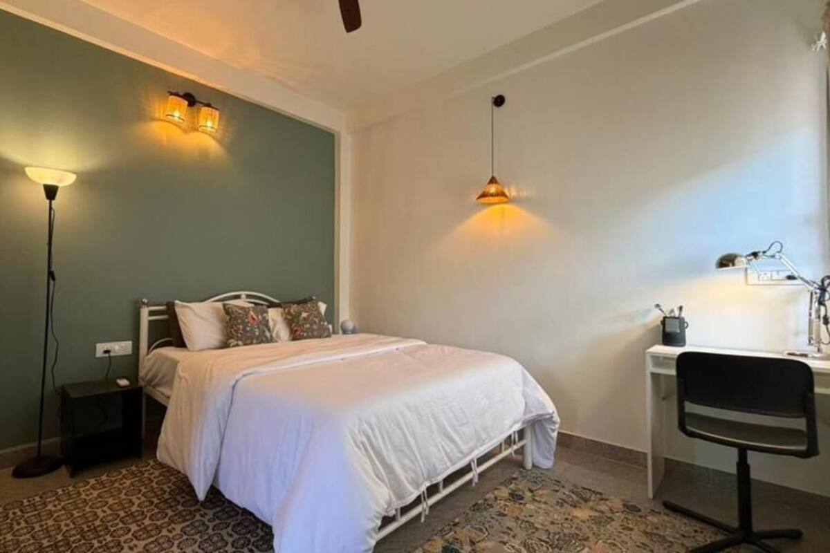 Un dormitorio con cama, mesita de noche, lámpara, escritorio, silla y una escalera.