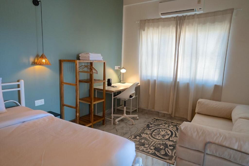 Un dormitorio con cama, escritorio y silla, armario y ventana con cortinas.