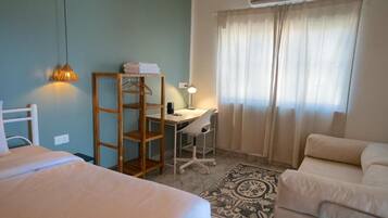 Un dormitorio con cama, escritorio y silla, armario y ventana con cortinas.