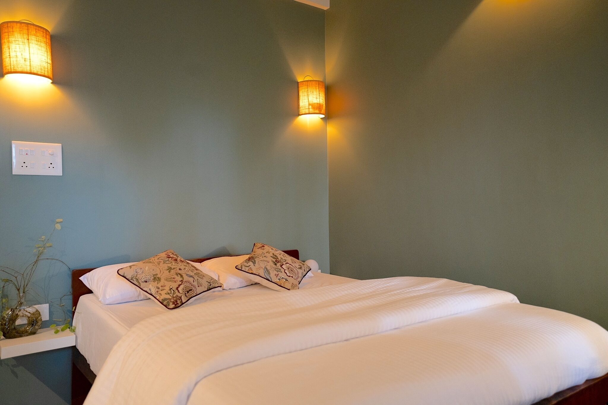 A bedroom with a bed, two wall-mounted lamps, and a power outlet on the wall.