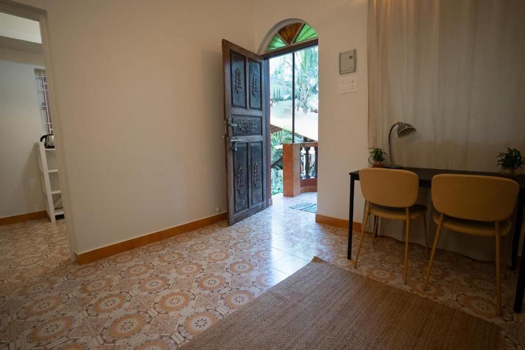 Un couloir doté d’un sol à motifs, une porte en bois, une petite table avec deux chaises et une vue sur un balcon.
