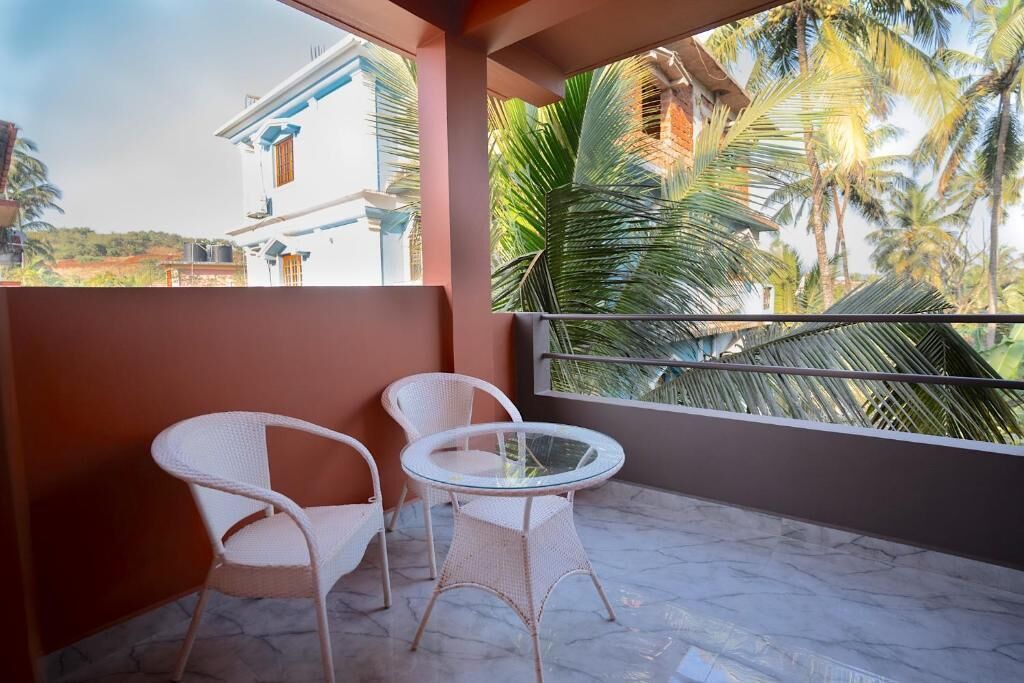 A balcony with two white wicker chairs and a glass table, overlooking a building and palm trees.