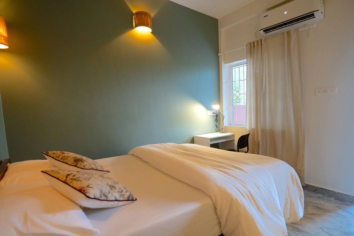 Un dormitorio con cama, escritorio, silla, lámpara y aire acondicionado.