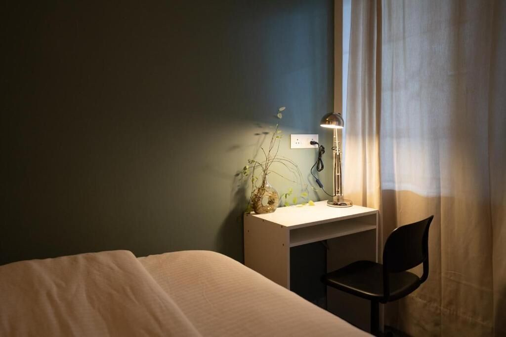 A bedroom with a bed, a desk with a lamp, a chair, and a window with curtains.