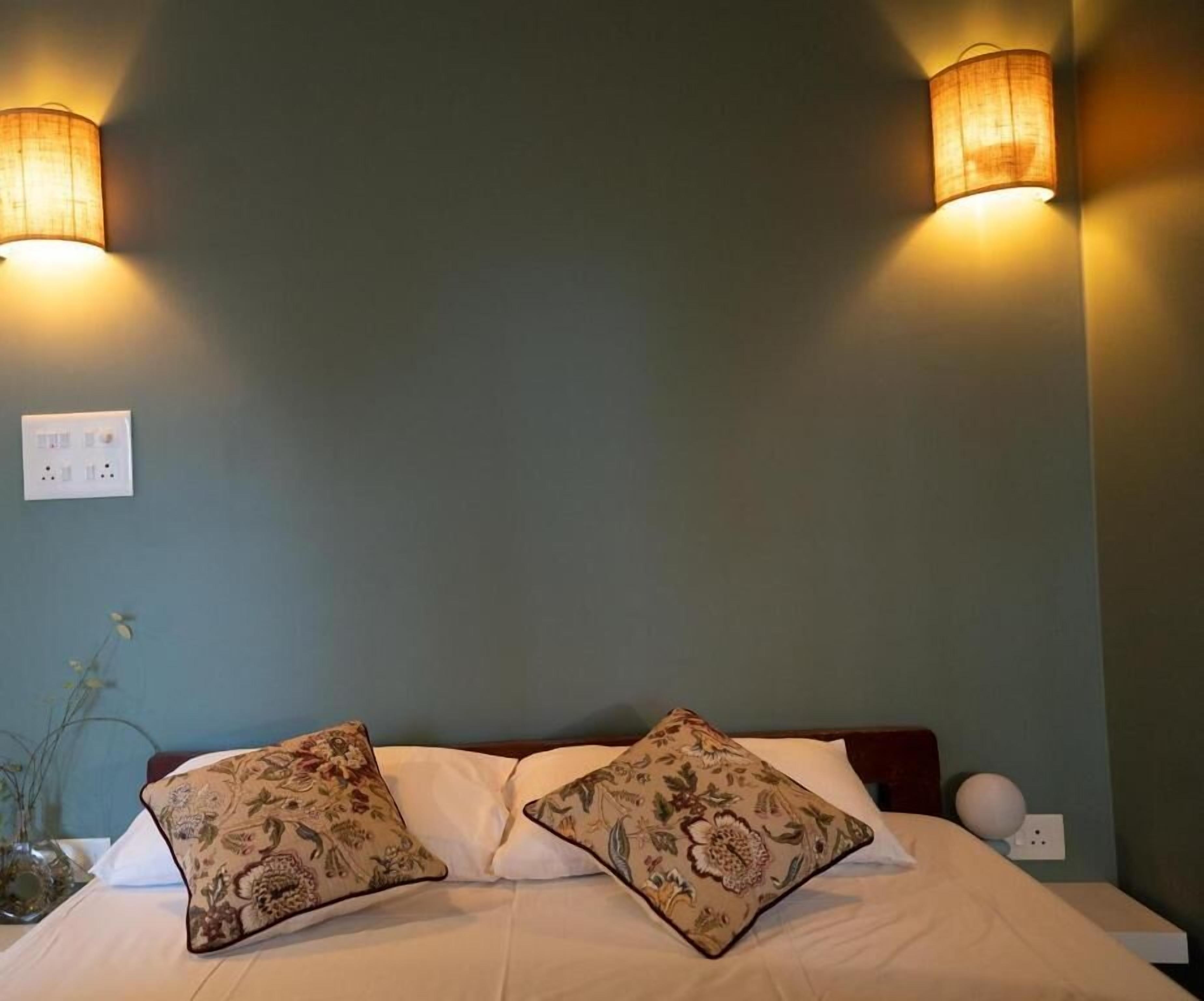 Un lit avec deux coussins à motifs, une table de chevet et deux lampes fixées au mur.