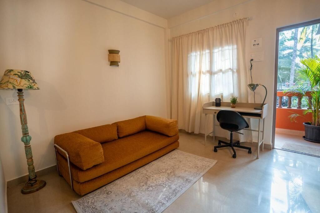 Une pièce comprenant un canapé, un bureau, une chaise, une lampe et une fenêtre avec des rideaux.