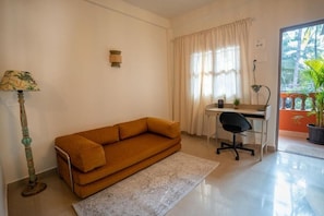 Una habitación con sofá, escritorio, silla, lámpara y ventana con cortinas.