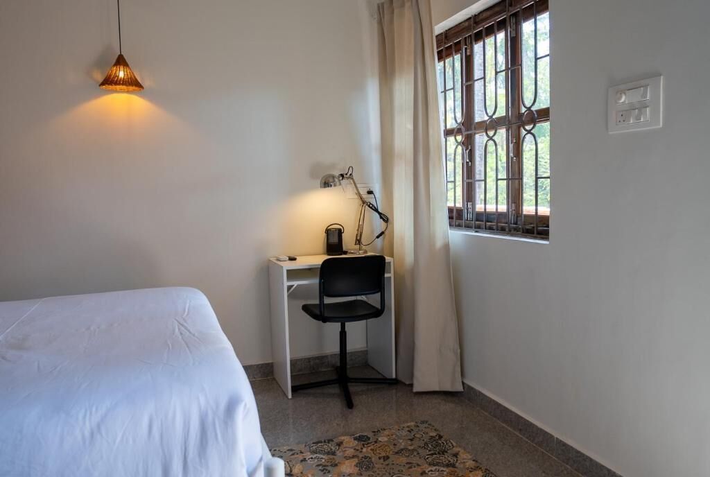 Une chambre à coucher avec un lit, un bureau avec une chaise, une lampe et une fenêtre avec des rideaux.