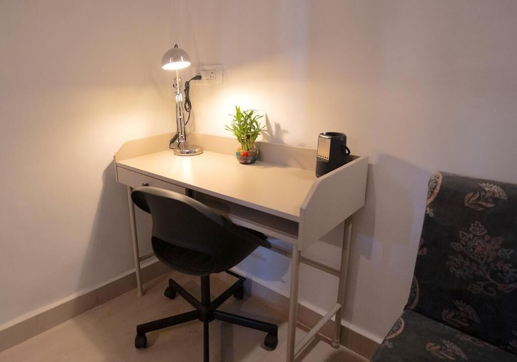 A small workspace with a desk, chair, lamp, potted plant, and a coffee maker.