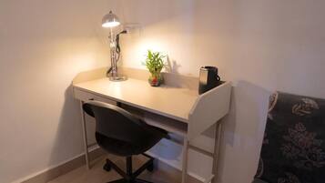 A small workspace with a desk, chair, lamp, potted plant, and a coffee maker.