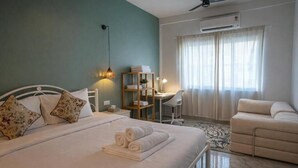 A bedroom with a bed, bedside tables, a desk, a chair, a sofa, a ceiling fan, and an air conditioning unit. - Wonderland  (Mandrem pernem)