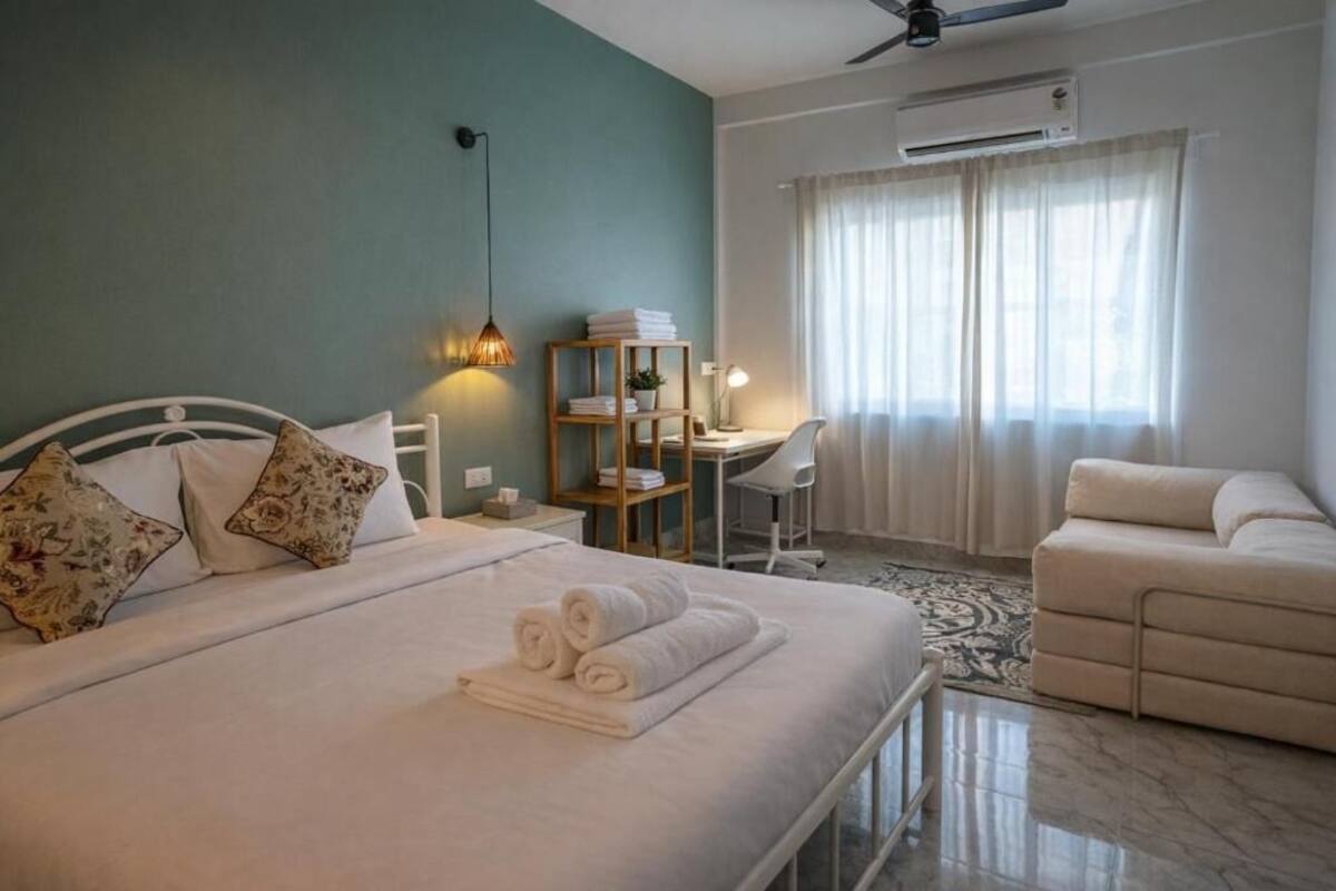 Un dormitorio con cama, mesitas de noche, escritorio, silla, sofá, ventilador de techo y aire acondicionado.