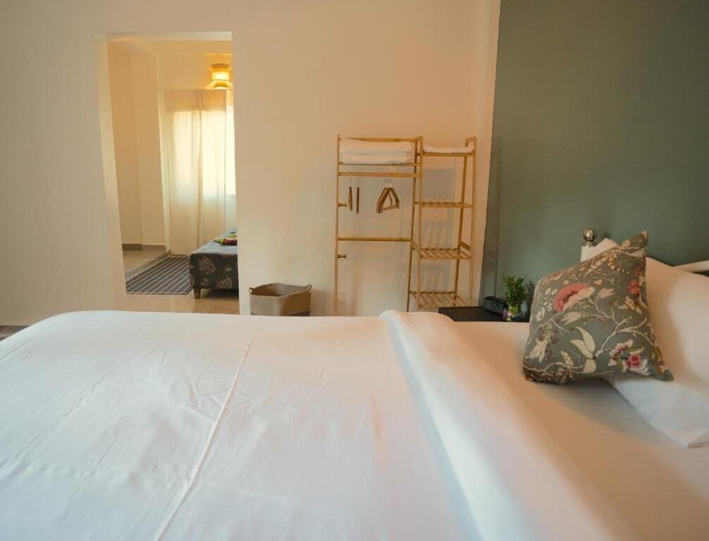 A hotel room with a large bed, a wooden rack with towels, and a view of another room.