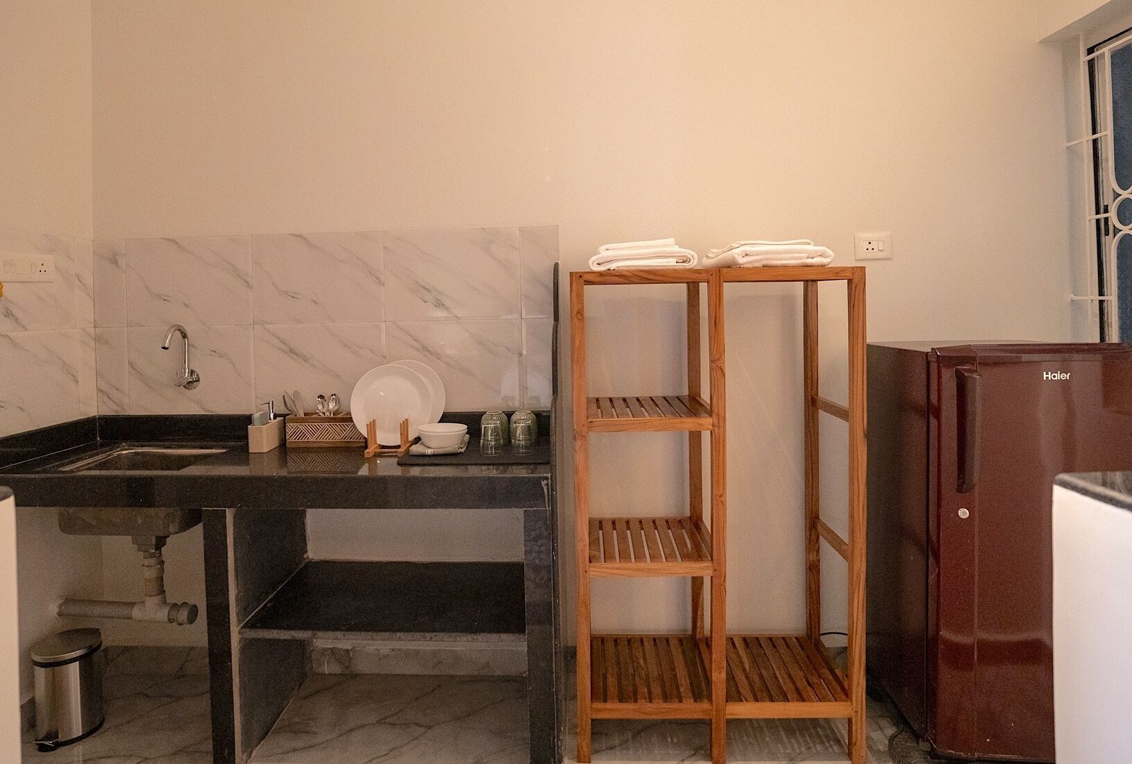 A kitchen with a marble backsplash, a sink, a wooden shelf unit, and a refrigerator.