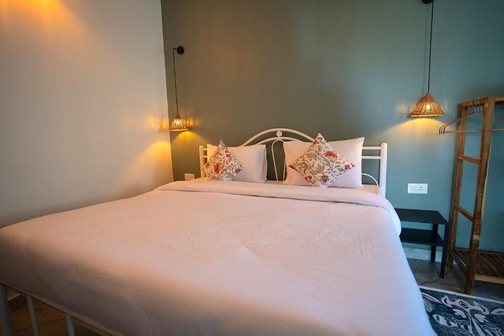 A neatly made bed with white bedding and floral pillows, a small bedside table, and two wall-mounted lamps.