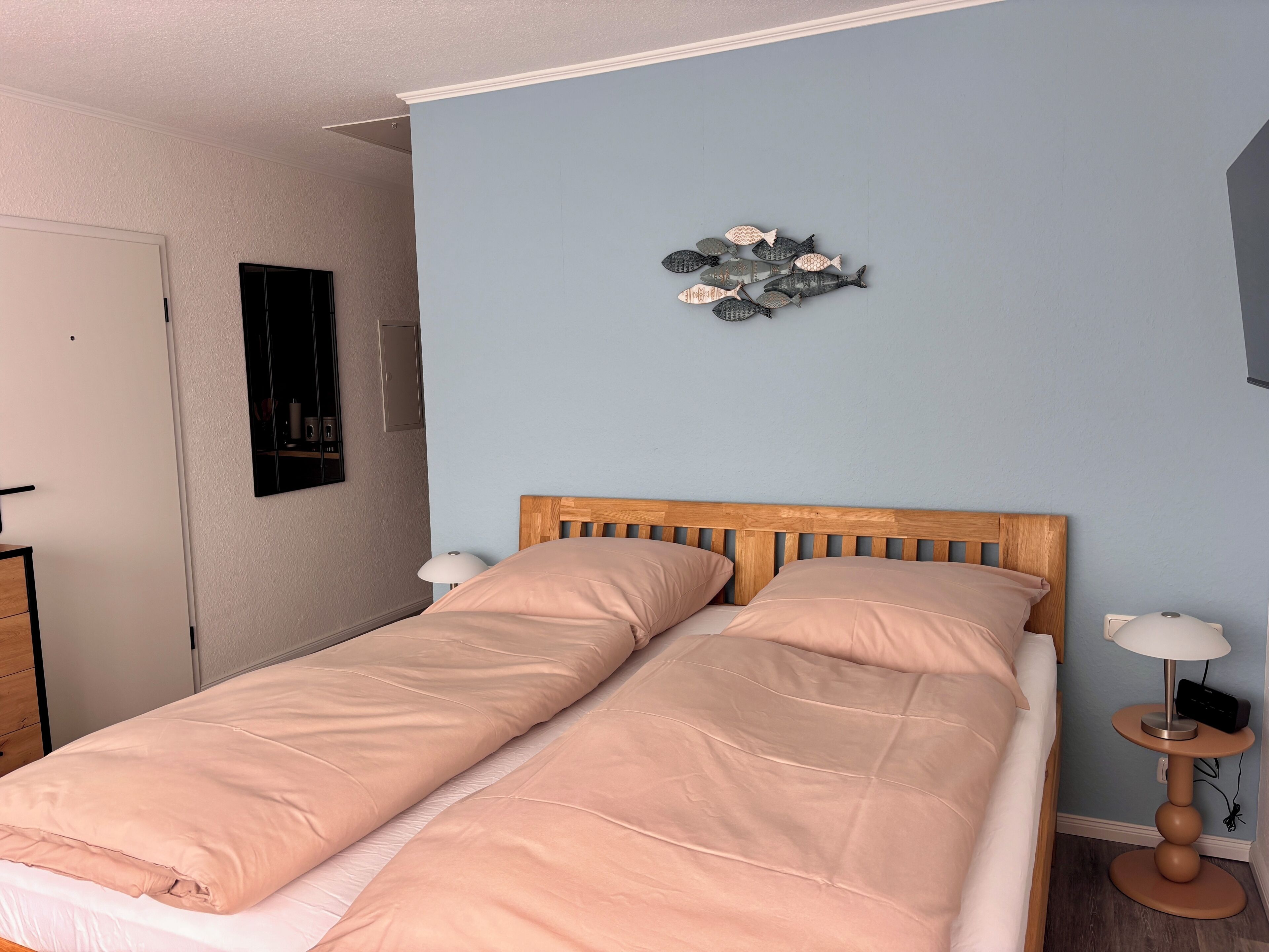 Un dormitorio con una cama, una mesita de noche con lámpara, un adorno en la pared y una puerta.