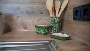 A kitchen with wooden cabinets, a green and white patterned container holding wooden utensils, and a green and white patterned baking dish. - studio no. 4 newly furnished modern vacation studio in Wöhrden near Büsum (Wöhrden)