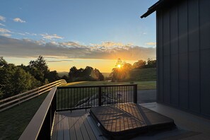 Une terrasse offrant une vue sur le coucher de soleil au-dessus d’un paysage verdoyant.