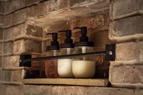 A shelf with three glass bottles and two pumps, likely for soap or lotion, mounted on a brick wall. - Luxe Mountain Getaway on Private Rd Near Rhinebeck (Hyde Park)