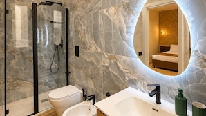 Un baño moderno con pared de mármol, un espejo grande, cabina de ducha y un bidé.