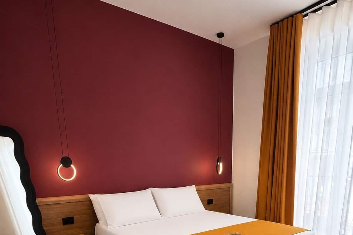 Quarto de hotel com cama, mesa de cabeceira, espelho e janela com cortinas.