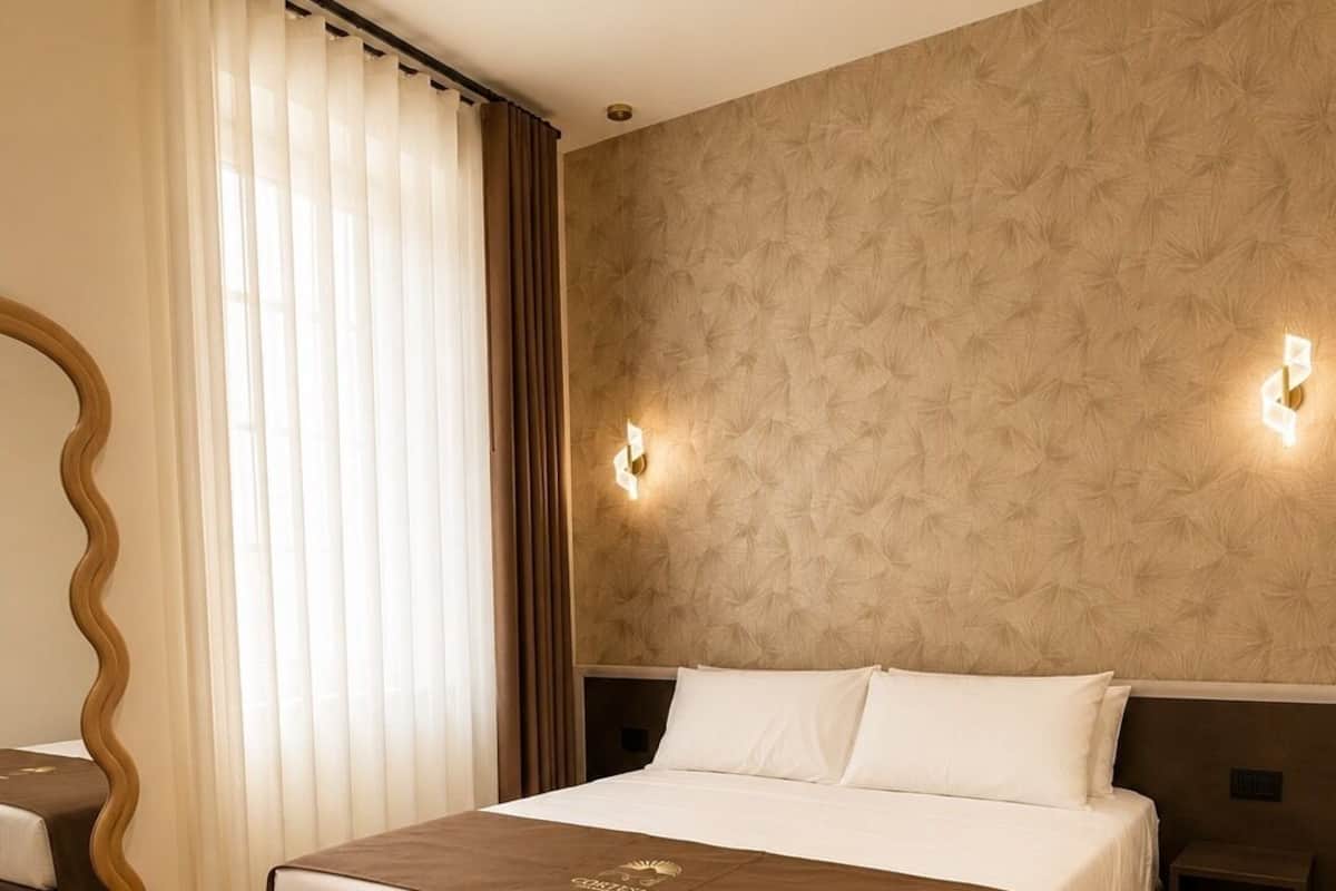 Quarto de hotel com uma cama grande, um espelho, uma mesa de cabeceira e uma luminária na parede.
