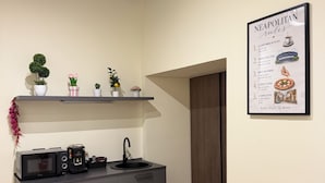 Una cocina moderna con microondas, cafetera y lavamanos. Hay plantas en macetas sobre un estante encima de la encimera. Un menú enmarcado con el título 'Neapolitan Rules' está en la pared.