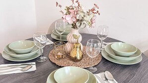 Ein runder Esstisch mit grünen Tellern, klaren Gläsern und einer Blumenvase.