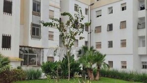 Um edifício com vários andares, varandas, área de jardim com palmeiras e fachada branca.