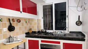 Uma cozinha com armários vermelhos, bancada preta, fogão, pia e uma janela.