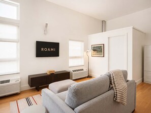 A modern living room with a grey sofa, a black TV, and a framed picture on the wall. - Roami at Studio 135 - Stylish Studio | 2 units (Denver)