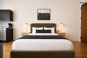 A neatly arranged hotel room with a bed, bedside tables, a coffee machine, and a cityscape artwork on the wall. - Roami at Studio 135 - Stylish Studio | 2 units (Denver)