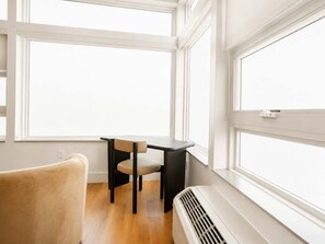 A room with a window, a chair, a table, and a wall-mounted heater. - Roami at Studio 135 - Stylish Studio | 2 units (Denver)
